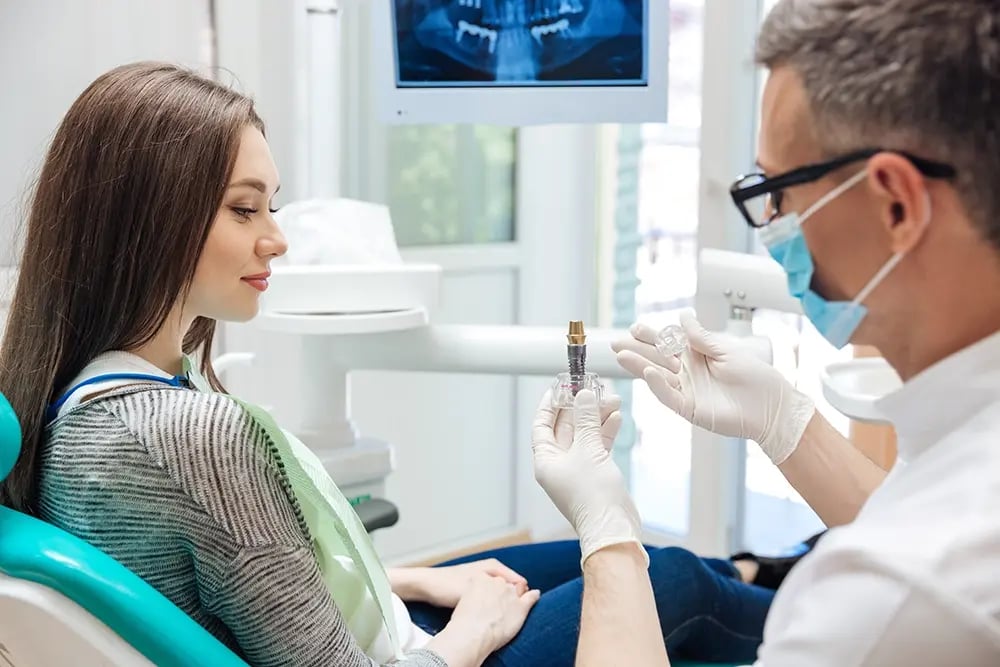 Médico explica ao paciente como os implantes dentários e a prótese personalizada permitem obter um sorriso com aspeto natural.