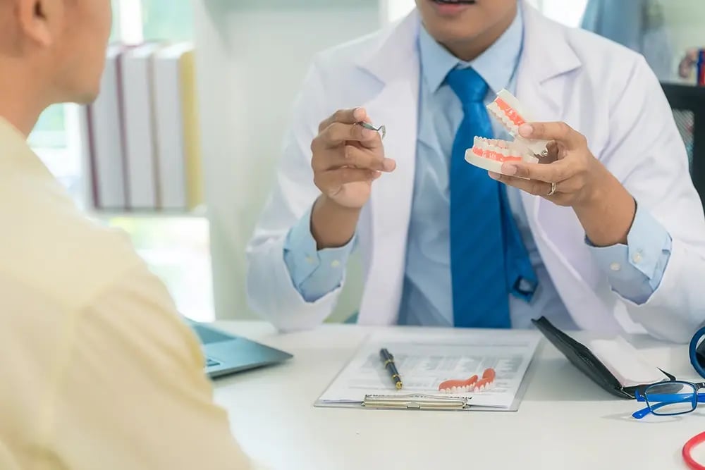 Médico dentista a explicar o tratamento com um modelo dentário durante a consulta.