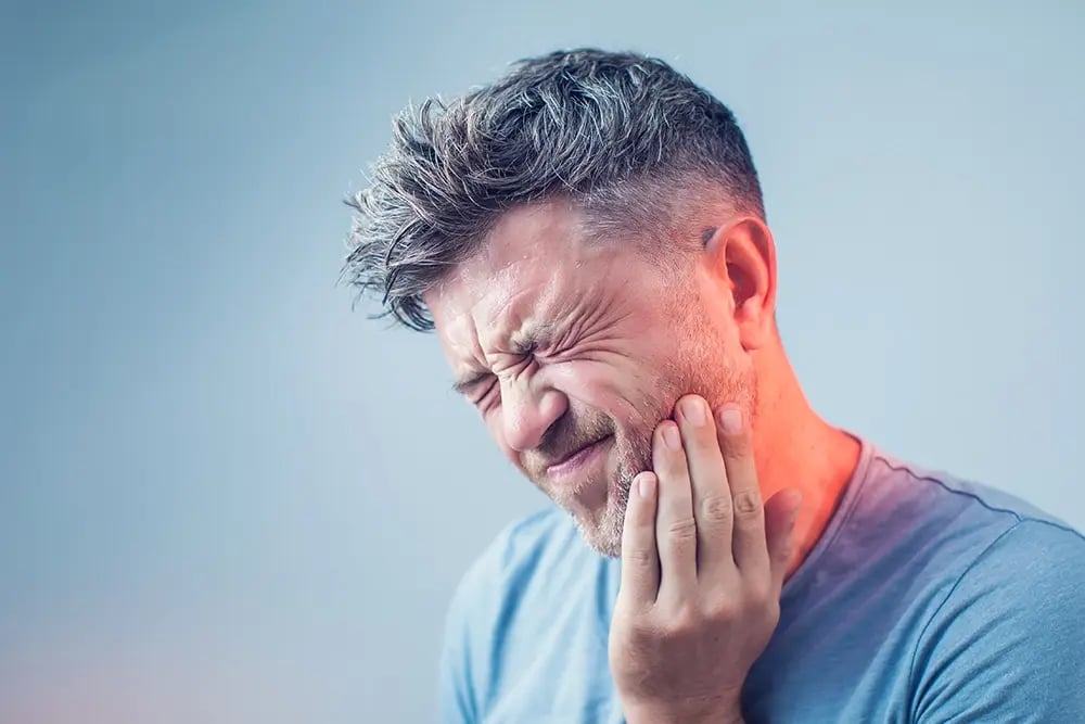 Homem com dor na mandíbula devido à perda dentária, ilustrando uma das situações que leva muitas pessoas a adiar a procura de informação sobre implantes dentários.