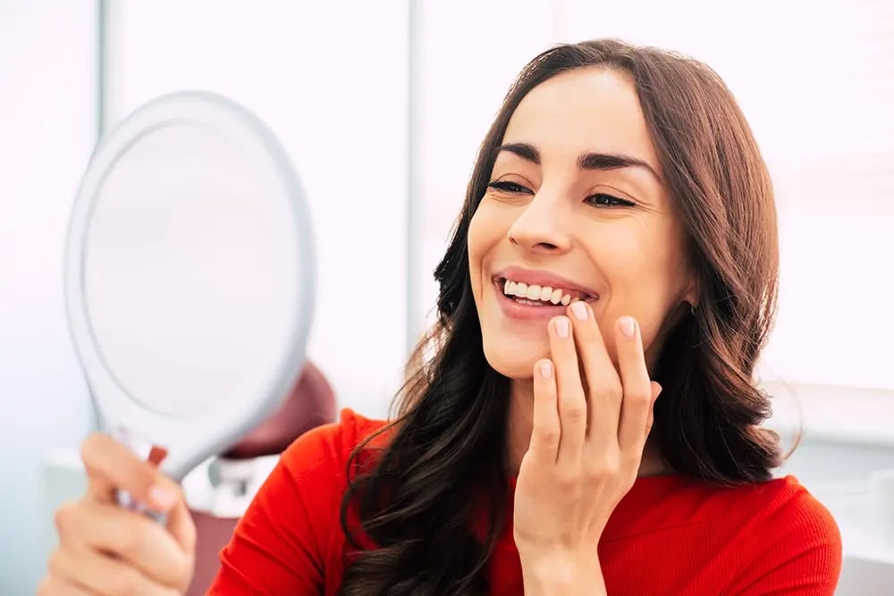 Paciente observa ao espelho o sorriso natural obtido através de uma reabilitação com implantes dentários personalizados.