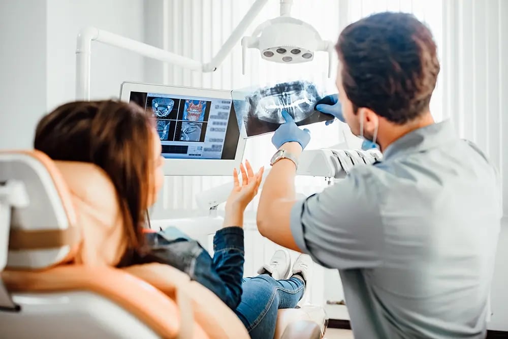 Médico dentista analisa uma radiografia dentária com a paciente durante a avaliação clínica para planear o tratamento com implantes.