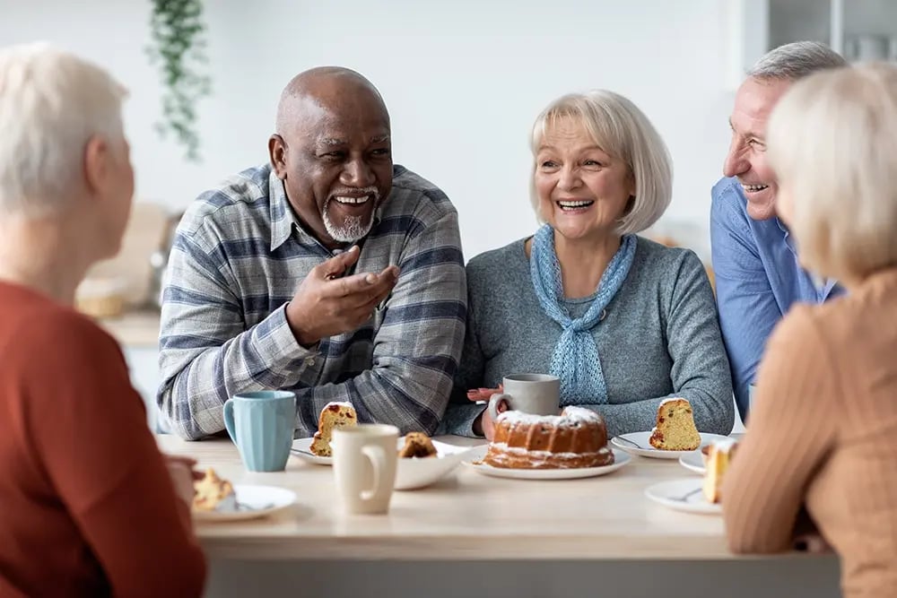 Pessoas seniores a sorrir e conviver à mesa com confiança e conforto.