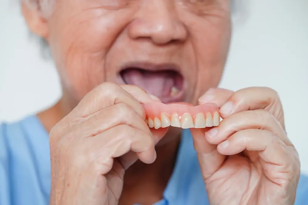 Paciente a colocar uma dentadura convencional removível na boca.