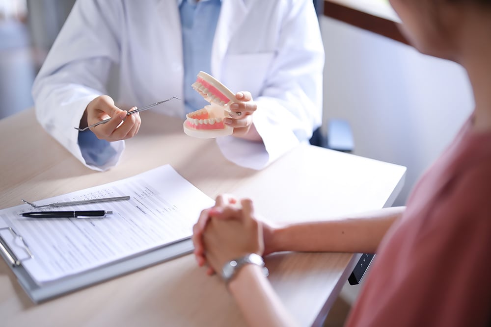 AdobeStock_984509623 copMédico dentista a explicar um tratamento utilizando um modelo dentário durante a consulta de avaliação.