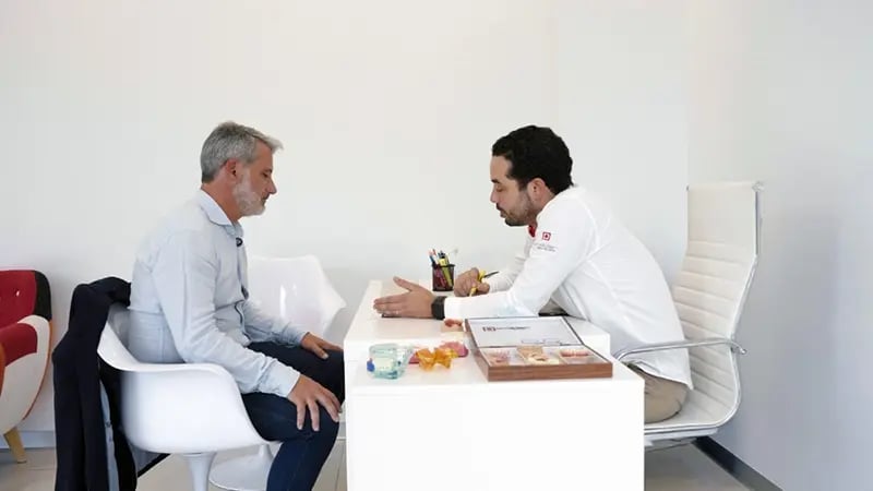Médico dentista explica o planeamento da cirurgia de implantes dentários durante a consulta de avaliação.